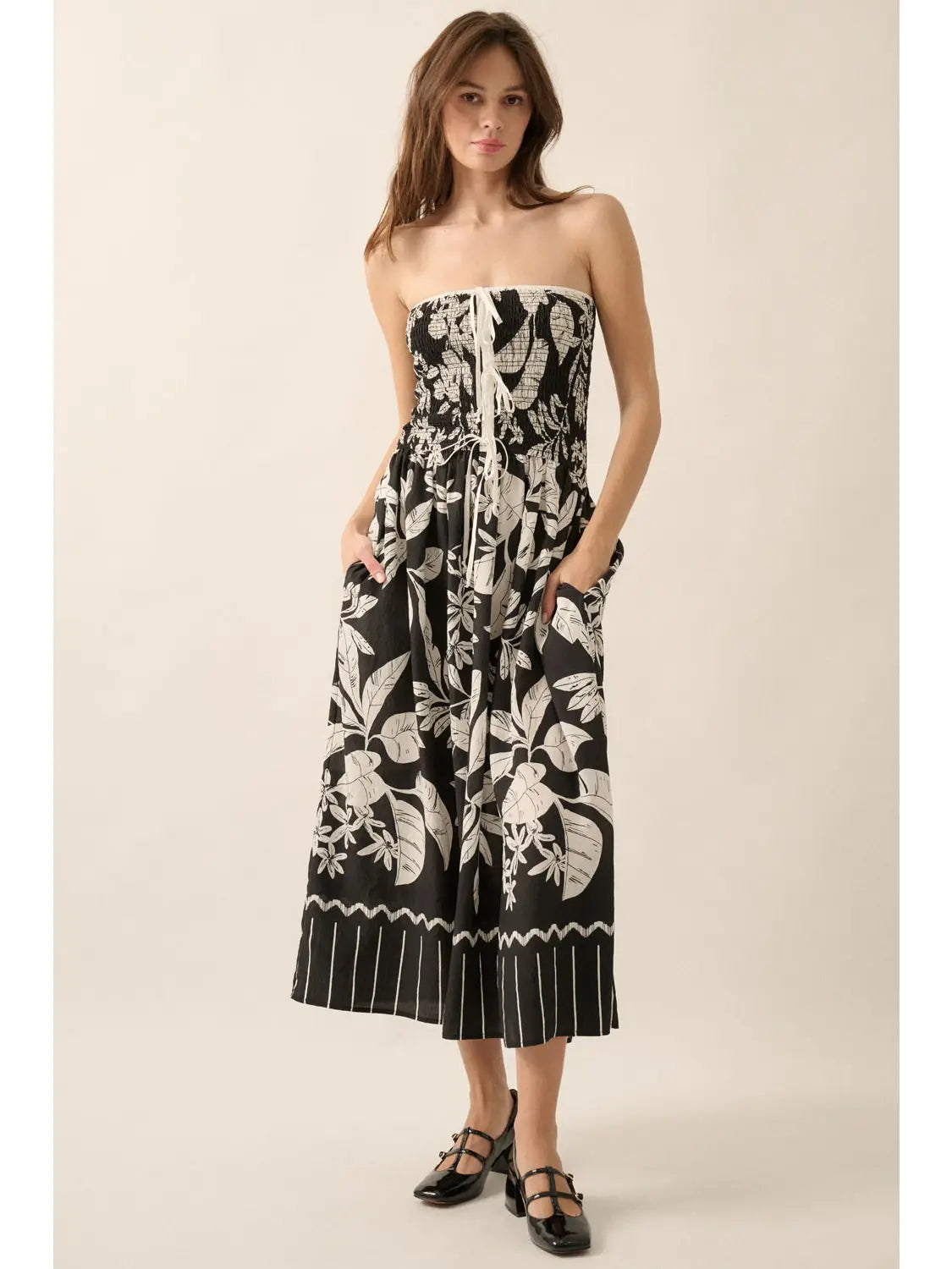 Woman wearing a black strapless dress with white floral pattern on a beige background