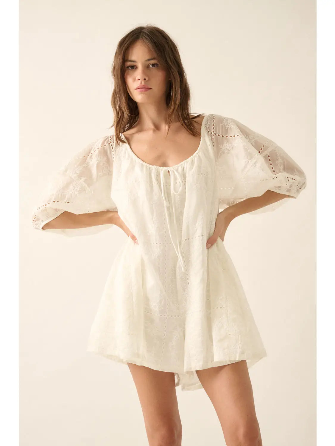 Woman wearing a white romper with sheer sleeves against a plain background