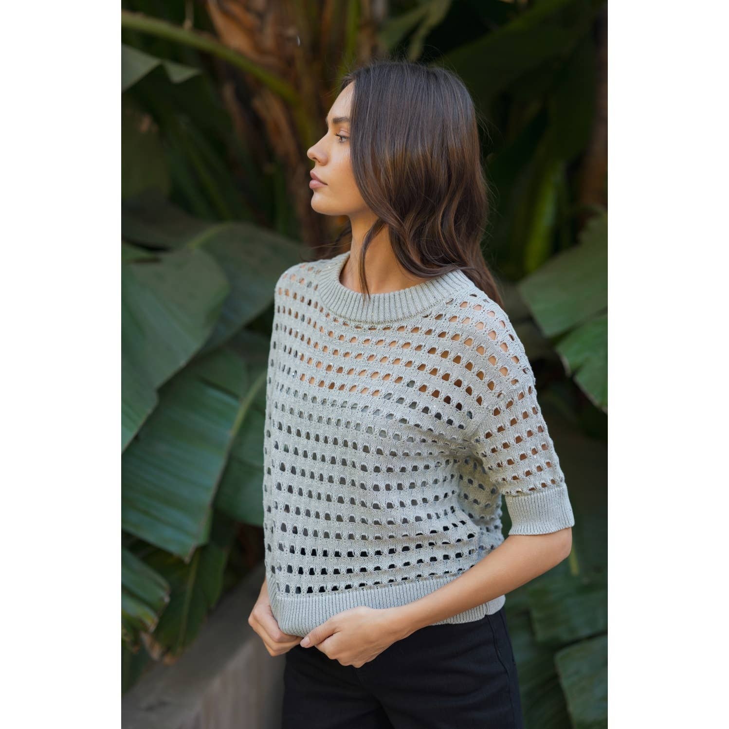 Woman wearing a light blue sweater with a pattern, standing in front of green foliage.